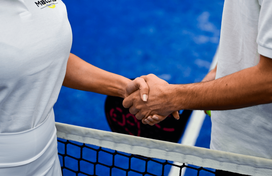 Two people shaking hands across a net on a blue padel court, showing sportsmanship.